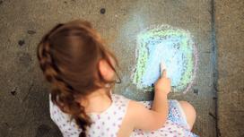Маленькая девочка рисует мелом на асфальте