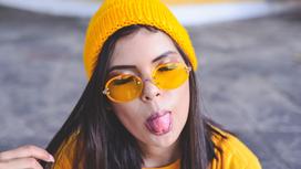 Девушка в желтой одежде показывает язык