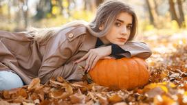 Девушка в кожаном плаще с тыквой лежит на ворохе осенних листьев