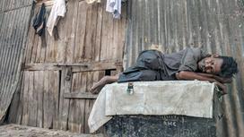 Мужчина в грязной одежде спит на улице возле сарая
