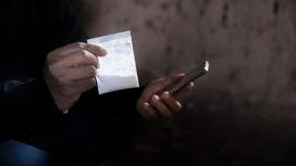 Мужчина держит в руках наркотики и телефон