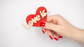 Женская рука с красным маникюром держит сердечко