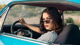 Женщина в солнцезащитных очках за рулем голубой машины