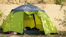 Зеленая купольная палатка стоит на песчаном грунте