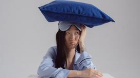 Девушка в пижаме и маске для сна с подушкой на голове
