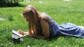 Девушка читает электронную книгу, лежа на траве