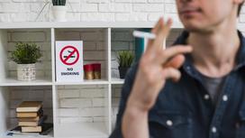 Мужчина курит на фоне запрещающей таблички