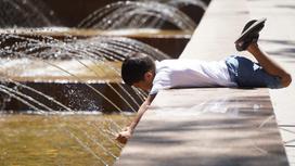 Мальчик лежит на бортике фонтана и трогает воду руками