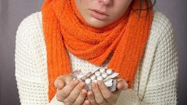 Девушка в шарфе держит лекарства в руках
