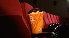 Упаковка с попкорном стоит на подлокотнике сиденья в кинотеатре