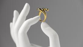 В гипсовой руке между пальцами закреплено золотое кольцо с фигурными завитушками