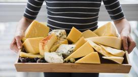 Женщина держит деревянный поднос с разными сортами сыра. Сыр нарезан кусками разной формы и размеров