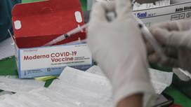 Человек держит шприц в руках на фоне коробки с вакциной Moderna