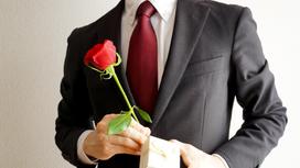 Мужчина в костюме стоит с розой и коробочкой с подарком