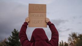 Девушка держит над головой плакат "Любовь не должна причинять боль"