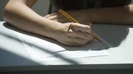 Человек сидит за столом и пишет карандашом на бумаге