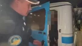 Полицейский в Павлодаре стоит рядом с автомобилем, в котором находится подозреваемый