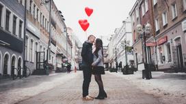 Парень и девушка стоят посреди улицы с тремя красными шариками в форме сердца