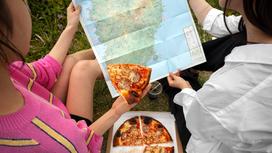 Молодые люди держат в руках карту и кусочек пиццы