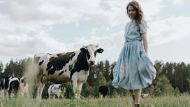 Девушка в голубом платье стоит в поле рядом с коровами