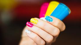 Женская рука с разноцветным маникюром держит флакончики с лаком для ногтей