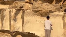 Мужчина выбивает надпись на скале