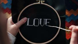 Девушка вышивает английское слово "любовь" на черной канве