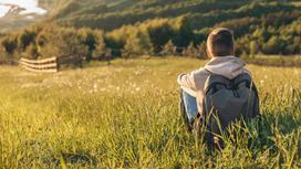 Подросток с рюкзаком сидит на траве