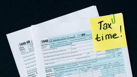 На столе лежат налоговые декларации и стикер Tax time!