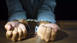 Мужчина держит руки в наручниках на столе