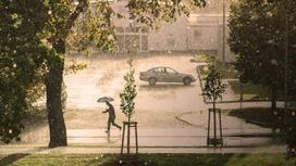 Человек с зонтом бежит по дороге во время сильного дождя