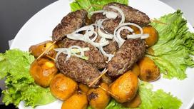 На сервировочной тарелке люля-кебаб с картофелем и листьями салата