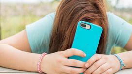Девочка-подросток закрыла лицо смартфоном