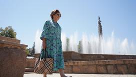 Пожилая женщина идет рядом с фонтаном