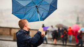 Мужчина пытается удержать зонт во время сильного ветра