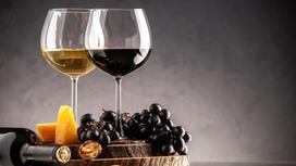 На деревянной подставке виноград, сыр и два бокала с вином