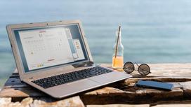 На фоне моря ноутбук, очки, телефон и бутылка