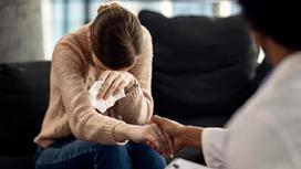 Женщина плачет, психолог держит ее за руку