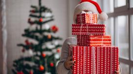 Девушка со стопкой упакованных в праздничную бумагу подарков на фоне новогодней елки