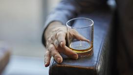 Мужчина придерживает пальцами руки бокал с виски