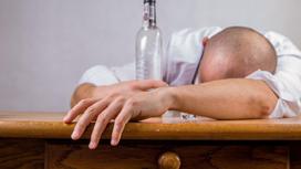 Пьяный мужик спит за столом с бутылкой в руках