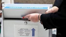 Женщина опускает бюллетень в ящик для голосования