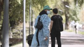 Женщина в защитной одежде и в маске на фоне парня на улице