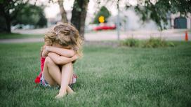 Девочка сидит на траве и закрыла лицо руками