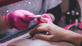 Мастер в розовых перчатках делает девушке маникюр