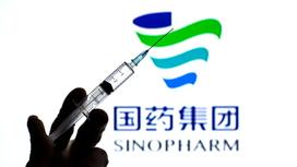 Шприц с жидкостью на фоне логотипа компании Sinopharm