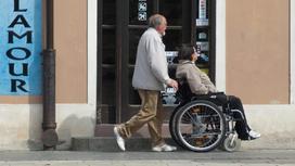 Мужчина везет женщину в инвалидной коляске