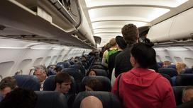 Пассажиры стоят в проходе на борту самолета