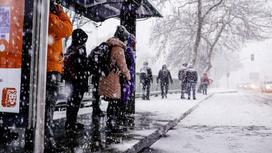 Люди стоят на остановке в снегопад