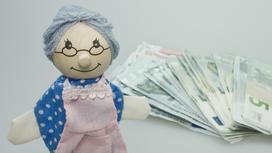 Игрушечная бабушка стоит на столе рядом с деньгами